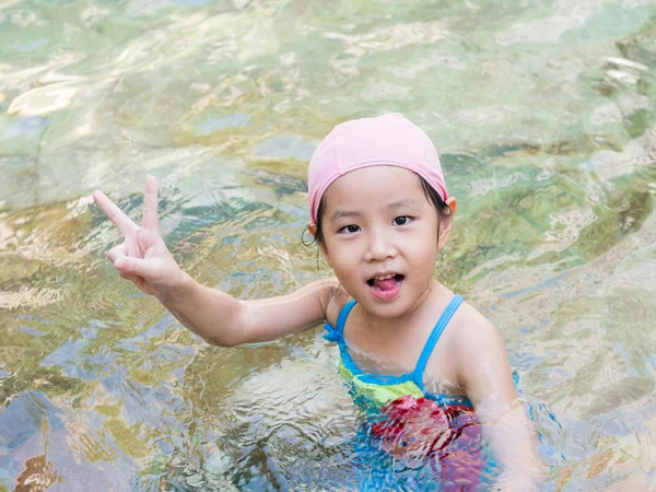 Asian girl is playing in the pool, victory fingers — Stock Photo, Image