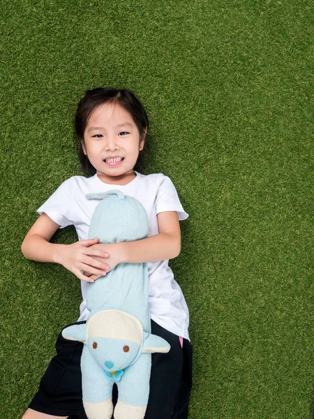 Маленькая азиатская девочка легла на лужайку со своей куклой — стоковое фото