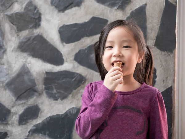 Маленькая азиатка ест мороженое, на фоне каменной стены — стоковое фото