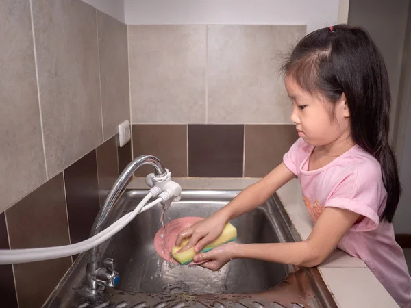 Adorable  kid girl washing dishes in domestic kitchen. Child hav — Stock Photo, Image