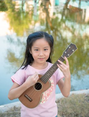 Küçük Asyalı kız ukulele çalıyor, bahçenin yanında.