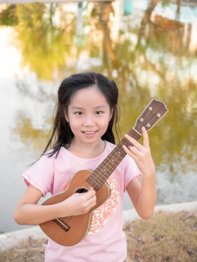Küçük Asyalı kız ukulele çalıyor, bahçenin yanında.