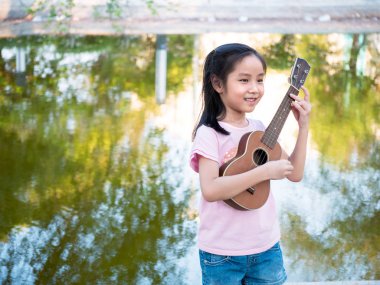 Küçük Asyalı kız ukulele çalıyor, bahçenin yanında.