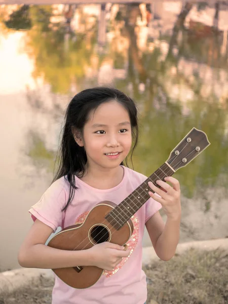 Malá asijské dítě dívka hrát ukulele, v zahradě v blízkosti Stock Fotografie