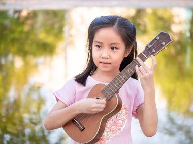 Küçük Asyalı kız ukulele çalıyor, bahçenin yanında.