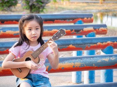 Küçük Asyalı kız, bahçede ukulele çalıyor.