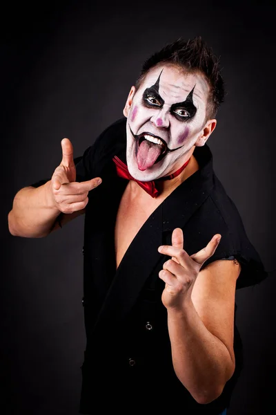 Evil clown, shows the tongue. The image for halloween. Studio photo on a black background