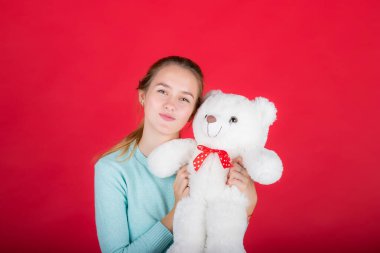 Genç beyaz kadın kırmızı arka planda beyaz bir oyuncak ayı tutuyor.