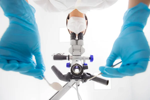 En kvinnlig tandläkare undersöker ett dentalt mikroskop. Bottenvy. — Stockfoto