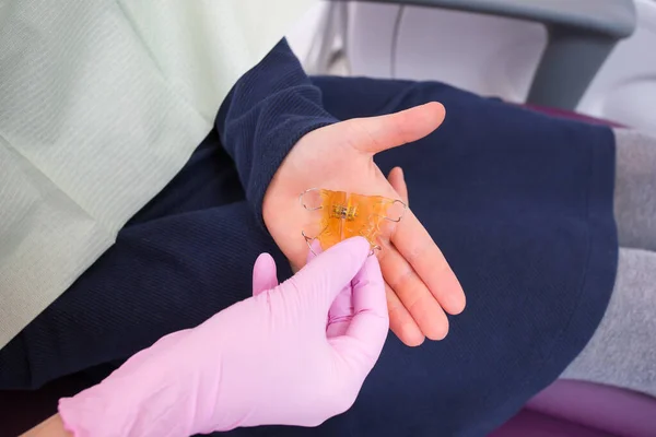 El dentista le da al niño una placa ortodóncica anatómica de acrílico naranja y metal en forma de mandíbula. Primer plano — Foto de Stock