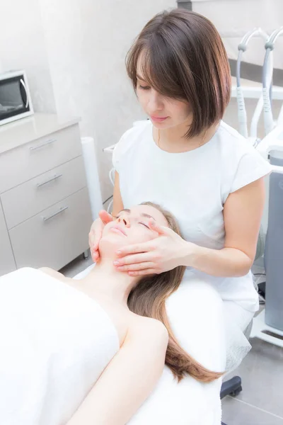 Giovane donna sulla procedura di ringiovanimento della pelle del viso. Estetista fa massaggio facciale con le mani . — Foto Stock