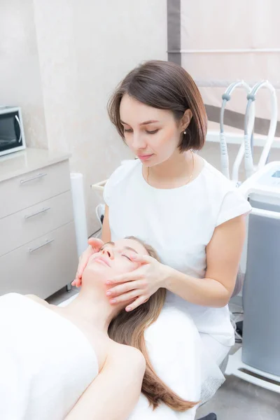 Jonge vrouw op gezichtsverjonging procedure. Beautician doet gezichtsmassage met handen. — Stockfoto