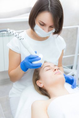 Güzellik uzmanı bir güzellik salonunda yatan kusursuz kadın yüzü için rf-lift işlemi yapıyor. Hasta yüz masajı yaptırıyor. Cilt tazeleme ve kırışıklık giderme.
