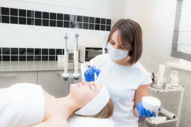 Güzellik uzmanı genç ve güzel bir müşterinin yüzüne doğal nemlendirici bir maske takar.