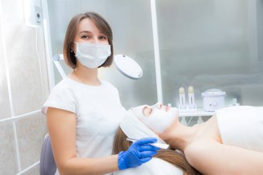 Güzellik uzmanı genç ve güzel bir müşterinin yüzüne doğal nemlendirici bir maske takar.