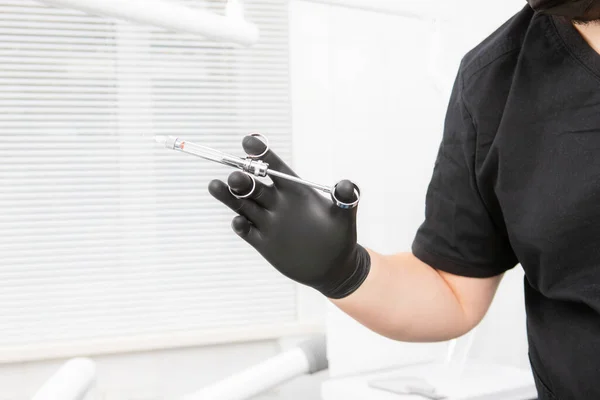 La mano del dentista en un guante negro sosteniendo una jeringa dental. para anestesia local — Foto de Stock