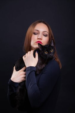 Siyah arka planda siyah elbiseli, kızıl saçlı genç bir kadın ve siyah bir kedi.