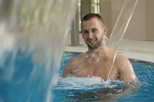 Schöner Mann genießt die Wassermassage im Wellnessbereich. — Stockfoto