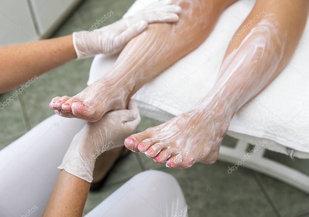 Female hands treating feet with moisturizing cream at beautician.