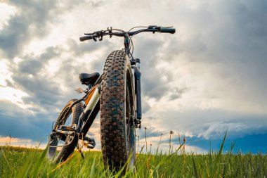 Kalın tekerlekleri olan bir bisiklet ve güzel bir gökyüzüne karşı yeşil bir çayırda elektrikli bir motor. Fatbike.