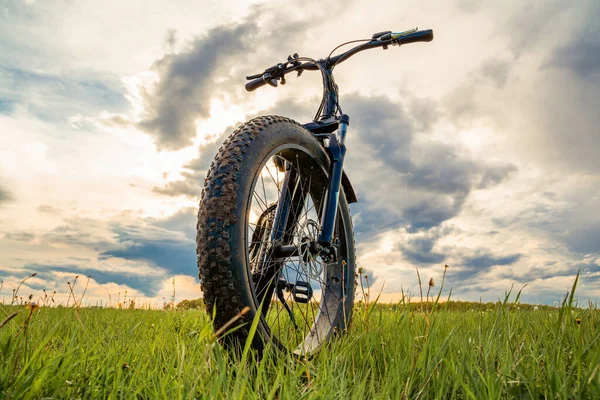 Güzel bir gökyüzüne karşı yeşil bir çayırda kalın tekerlekleri olan bir bisiklet. Fatbike.