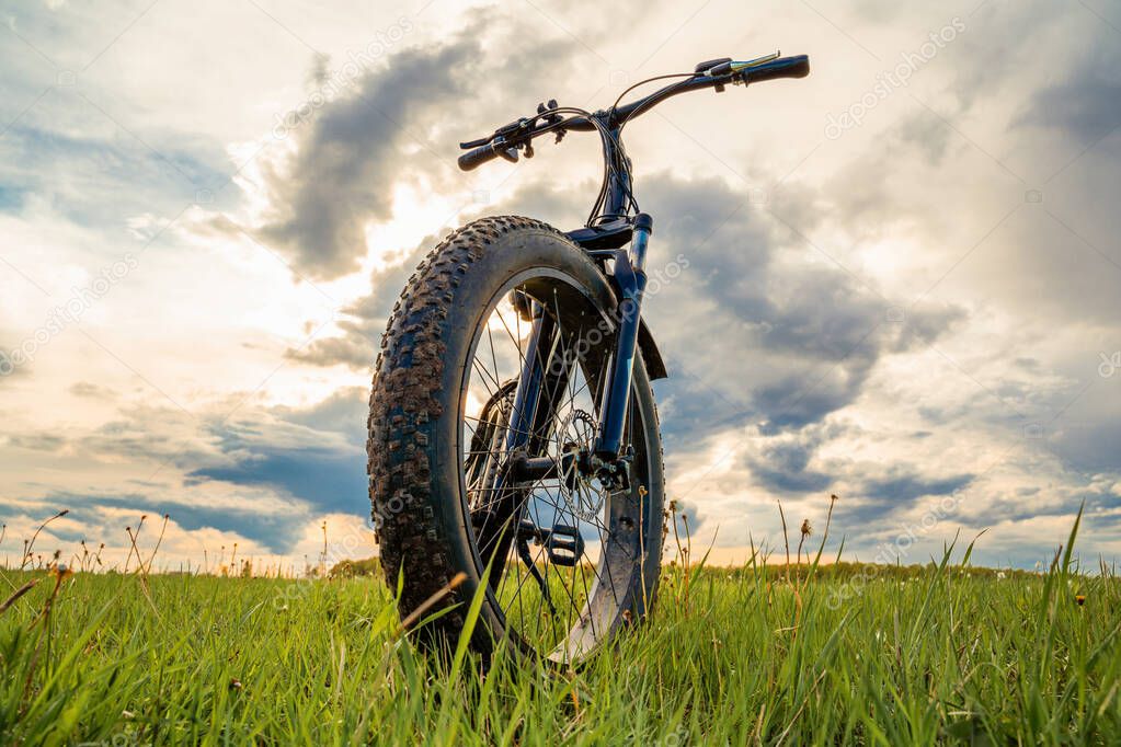 A Bicycle with thick wheels on a green meadow against a beautiful sky. Fatbike.