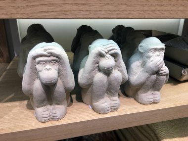 Maymun şeklinde şekillendirilmiş dekoratif çimento figürü. Bir mağazanın ahşap rafında üç bilge maymun figürü. Modern bir iç mekan için fikirler. Moda dekoru. Dinle, şeytanı görme.