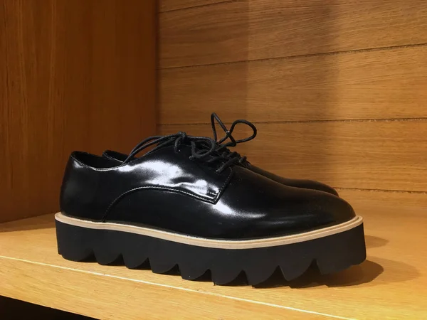 Black leather platform shoes. Burgundy classic shoes on a high black tractor platform on a wooden shelf in the closet. Fashionable Strict low-heeled shoes. Women Loafers with lacing