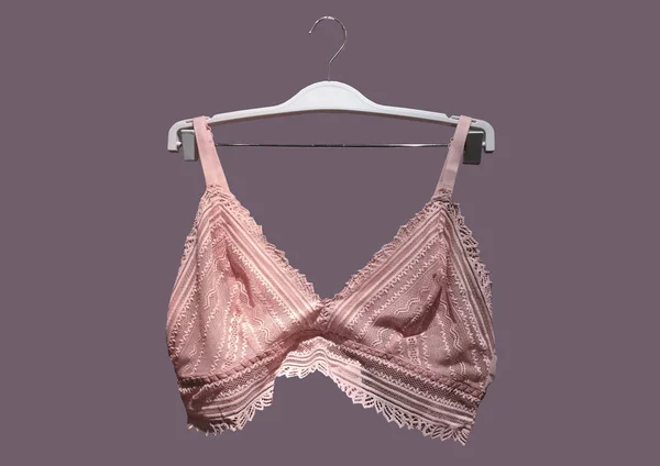 Menekşe arkaplanda izole edilmiş bir askıda pembe dantel sütyen. Tekstil, iç çamaşırı. Klasik Beyaz Dantelli Sütyen, çizilmemiş dantel ayrıntı. Cinsellik ve baştan çıkarıcı iç çamaşırı. Moda konsepti. Şık iç çamaşırı.