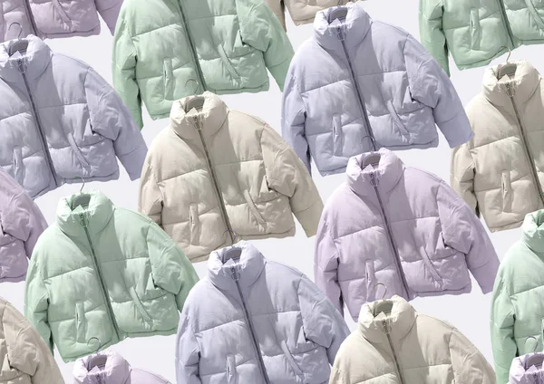 Multi colored women fashion down jacket pattern. A selection of different jackets on hangers isolated on beige background. Winter clothes pattern. Composition of clothes. Flat lay. Padded coat