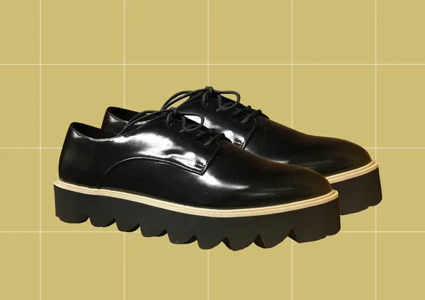 Black leather platform shoes isolated on yellow background. Classic shoes on a high black tractor platform. Fashionable Strict low-heeled shoes. Women Loafers with lacing. Composition of clothes