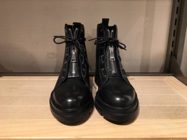 Rafta toka detaylarıyla siyah düz çizme. Kitle marketi. Modern kadın ayakkabıları satışı. Beton zeminde motorlu çizmeler, kemer tokalı sivri uçlu ayak parmaklı punk stili 