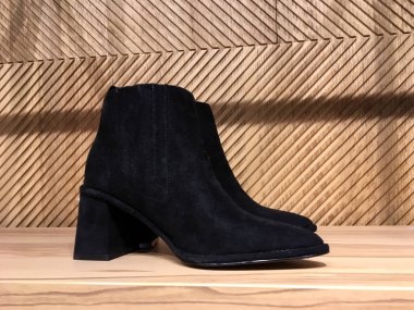 Rafta siyah süet çizmeler var. Ahşap arka planda lüks bir mağazanın vitrininde şık ayakkabılar. Modaya uygun kadın ayakkabılarının tanıtımı. Kitle marketi. Modern kadın ayakkabıları satışı