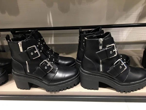 Black flat ankle boots with buckle details on the shelf. Mass market shop. Sale of modern women\'s shoes. Biker Boots Buckle Strap Pointed Toe Punk Style on a concrete background