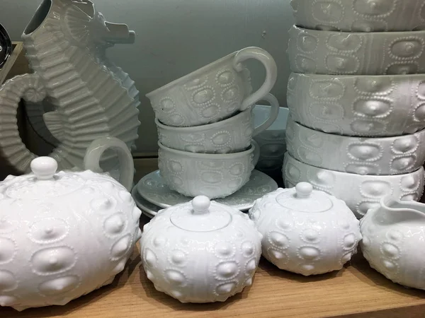 White designer ceramic dishes on a shelf in the closet. Seahorse-shaped porcelain jug. Pottery Shop. Designer ceramic dishes. Ceramic tableware top view. Modern empty round clean deep bowls. Household