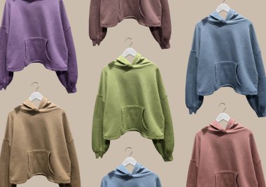 Kahverengi arka planda izole edilmiş askılarda çok renkli kapüşonlu kazaklar. Kıyafet kompozisyonu. Düz yatıyordu. Asgari düzeyde. Kıyafet kompozisyonu. Şablon. Moda kıyafet kolajı. Kapüşonlu