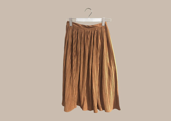 Beige pleated long skirt isolated on brown background pattern. Women's Elastic Waist Band Pleated Retro Maxi Long Skirt Dress. Long Accordion Pleated Skirt. Composition of clothes. Flat lay, top view