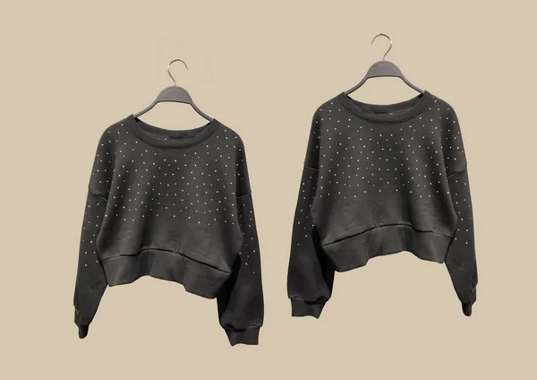 Black round neck sweatshirts with long sleeves and metallic stud appliques on hangers isolated on brown background. Composition of clothes. Flat lay. Minimal style. Composition of clothes. Pattern