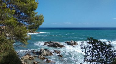 Dalgalar İspanyol sahilindeki kayalık bir plaja doğru ilerliyor. Sıcak güneşli bir gün