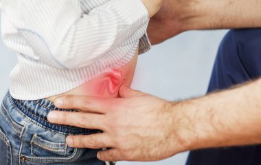 Doktor çocuğu muayene eder, göbeğine ve fıtığına bakar, mideye bakar ve izole edilmiş mavi bir arkaplanı kontrol eder.