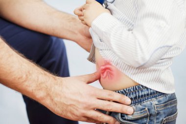 Doktor çocuğu muayene eder, göbeğine ve fıtığına bakar, mideye bakar ve izole edilmiş mavi bir arkaplanı kontrol eder.