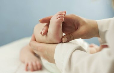Anne küçük bebeğinin ayaklarını tutarak, yakından anneyi sever. Bir doktor tarafından yapılan cilt muayenesi hariç.