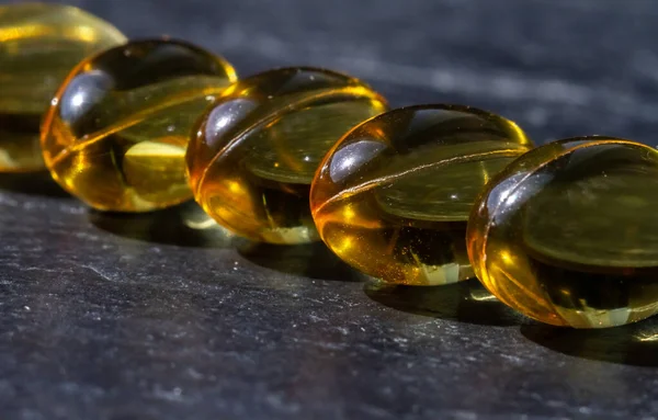 Birkaç vitamin ve mineral kapsülü ve balık yağı koyu bir arka planda üst üste yığılmış. Sağlık ve Beslenme İlaveleri