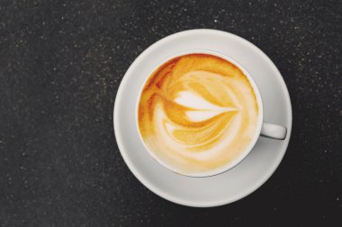 Beyaz seramik fincanda taze sıcak kapuçino kahve ve siyah arka planda güzel bir latte sanatı..