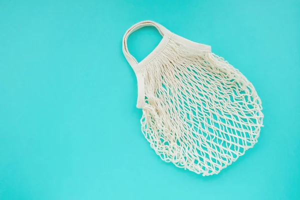 Reusable cotton net bag for shopping and food storage on mint background with copy space.