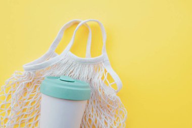 Market alışverişi, yiyecek depolama ve pastel sarısı arka planda bambu kupası için yeniden kullanılabilir çevre dostu pamuk ağı torbası. Kapatın. Uzayı kopyala Sıfır atık ve sürdürülebilir yaşam tarzı. Düz yatış, üst görünüm.