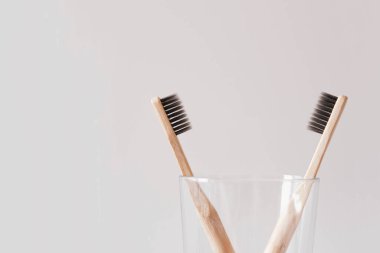 Havalı çevre dostu doğal bambu diş fırçaları bir bardakta, beyaz arka planda banyoda. Ağız temizliği kavramı. Mesaj için yer var. Plastik atıkları ve sürdürülebilir yaşam tarzını azaltır.