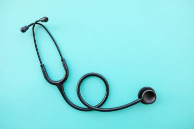 Açık mavi arka planda siyah modern steteskop. Tıp ve sağlık, kardiyoloji, tıp eğitimi. Akustik tıbbi cihaz. Mesaj için yer var. Düz-yatay, üst görünüm.