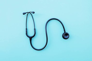 Açık mavi arka planda siyah modern steteskop. Tıp ve sağlık, kardiyoloji, tıp eğitimi. Akustik tıbbi cihaz. Mesaj için yer var. Düz-yatay, üst görünüm.