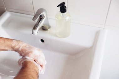 El yıkama konsepti. Adam banyoda sıvı dezenfektan sabun ve su kullanarak ellerini temizliyor. Kişisel hijyen, sağlık hizmetleri ve koronavirüs önleme.